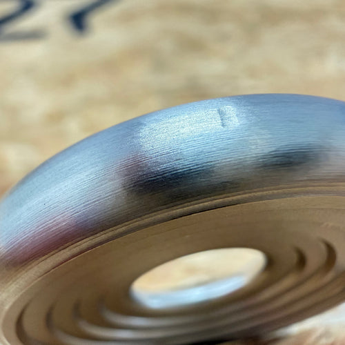 A close up of a 316 stainless coin-shaped object with concentric grooves and a hollow center, set against a blurred wood backdrop.
